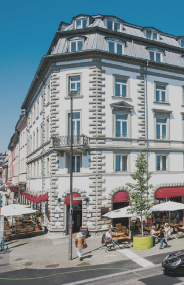 Belebtes Außenrestaurant direkt vor einem Eckhaus mit weißer Fassade