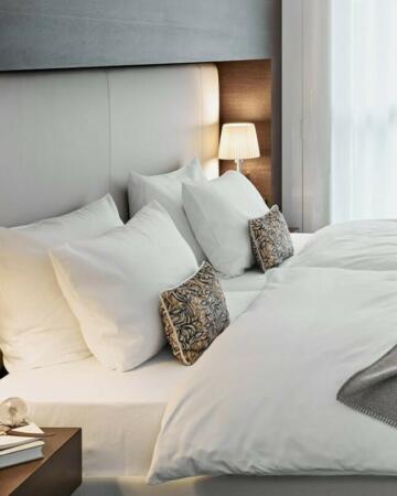 Modernes Hotelzimmer mit einem schlicht designten Bett mit weißem Bezug und gemütlicher Beleuchtung