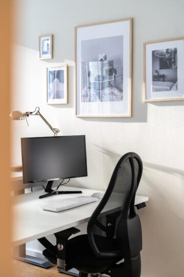 Online Birds Büro mit einem Schreibtisch, Bildschirm, Stuhl sowie einigen Bildern an der Wand