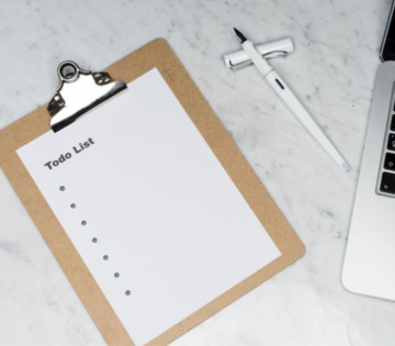 Schreibbrett mit einer ToDo Liste liegt neben einem offenen Füller auf einem weißen Marmortisch