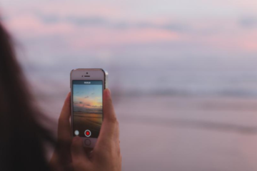 Frau die mit ihrem Handy den Sonnenuntergang am Meer filmt