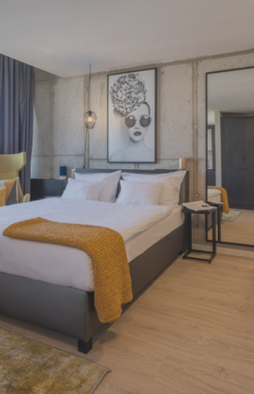 Hotelzimmer mit Betonwänden und einigen gelben Elementen sowie einem Bild über dem Bett